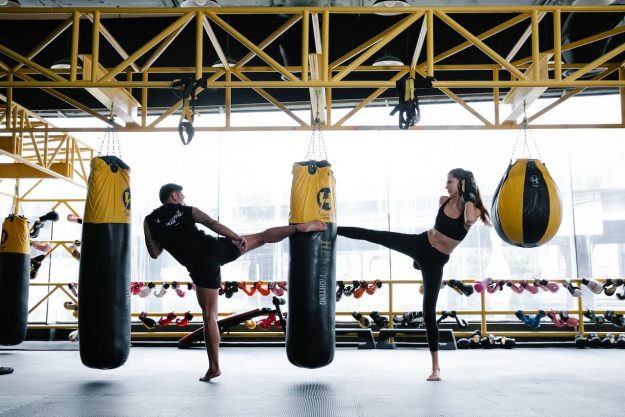 Imagen de un hombre y una mujer pateando simultáneamente el mismo saco de boxeo, mostrando su dedicación y destreza en el entrenamiento de artes marciales